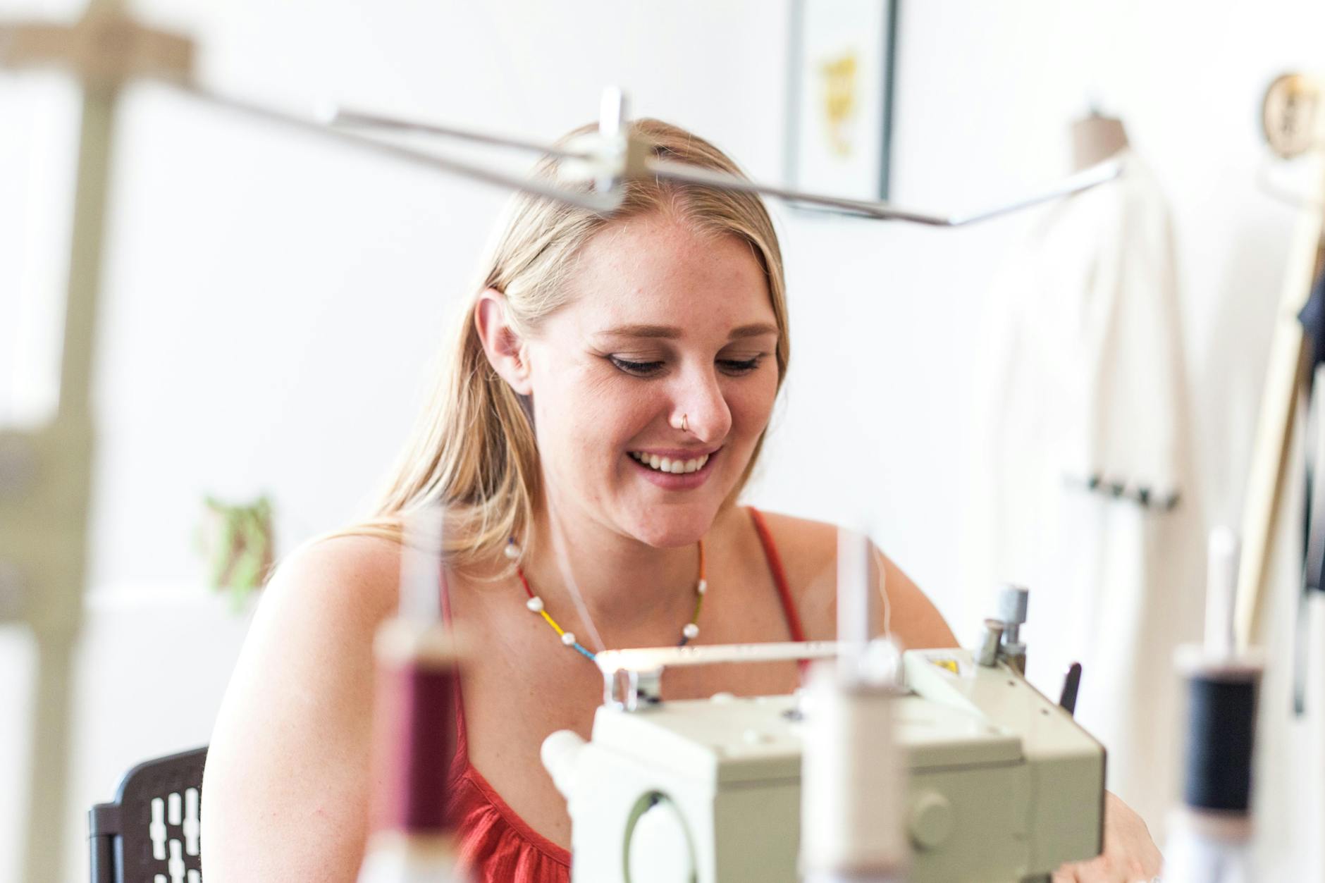 Uśmiechnięta kobieta szyje na maszynie w jasnym, domowym kąciku pracy