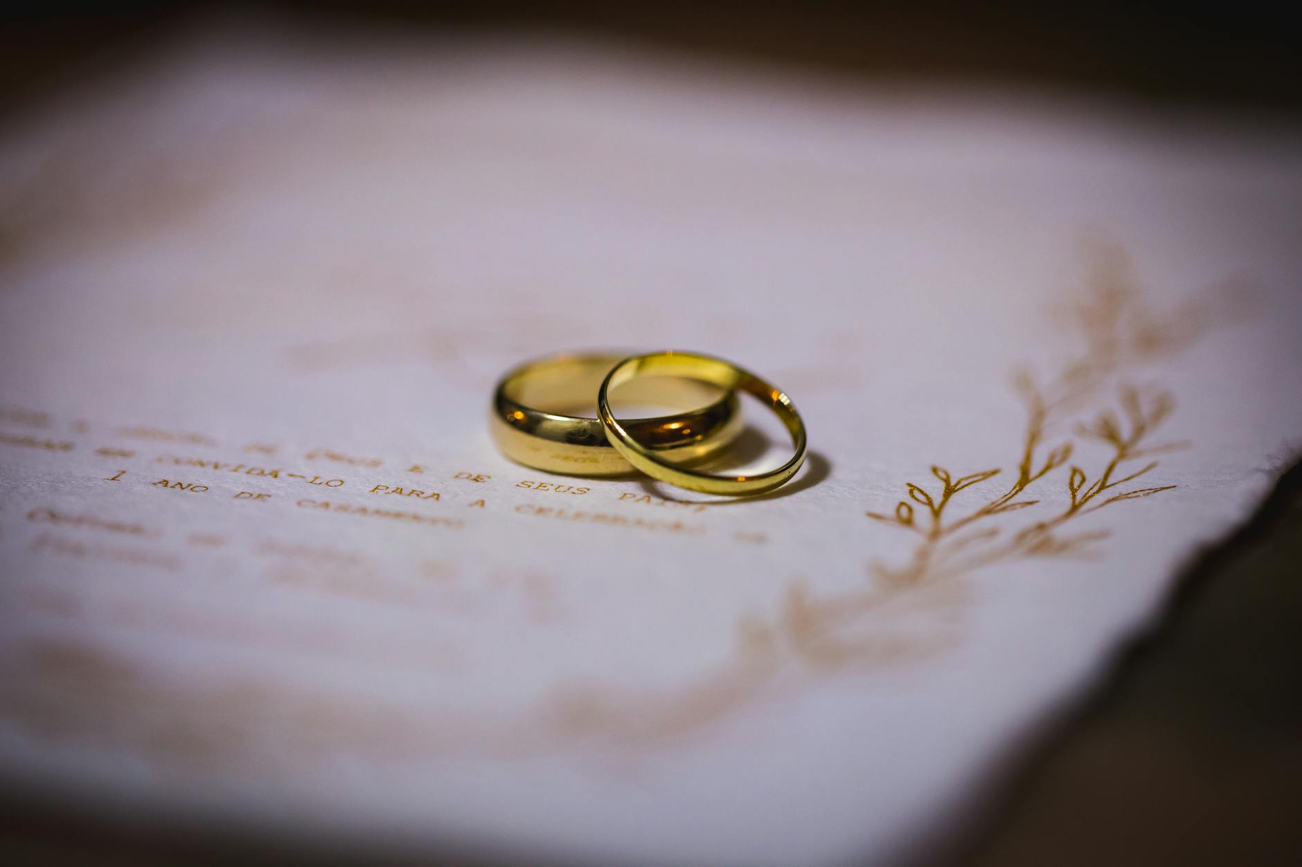 Zaproszenia na rocznicę ślubu w domu: jak napisać, żeby było serdecznie i konkretnie Złote obrączki położone na eleganckim zaproszeniu rocznicowym