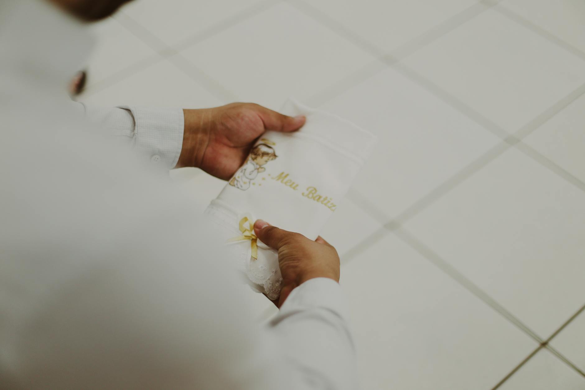 Dłonie trzymają białą chustę z złotym napisem na chrzest