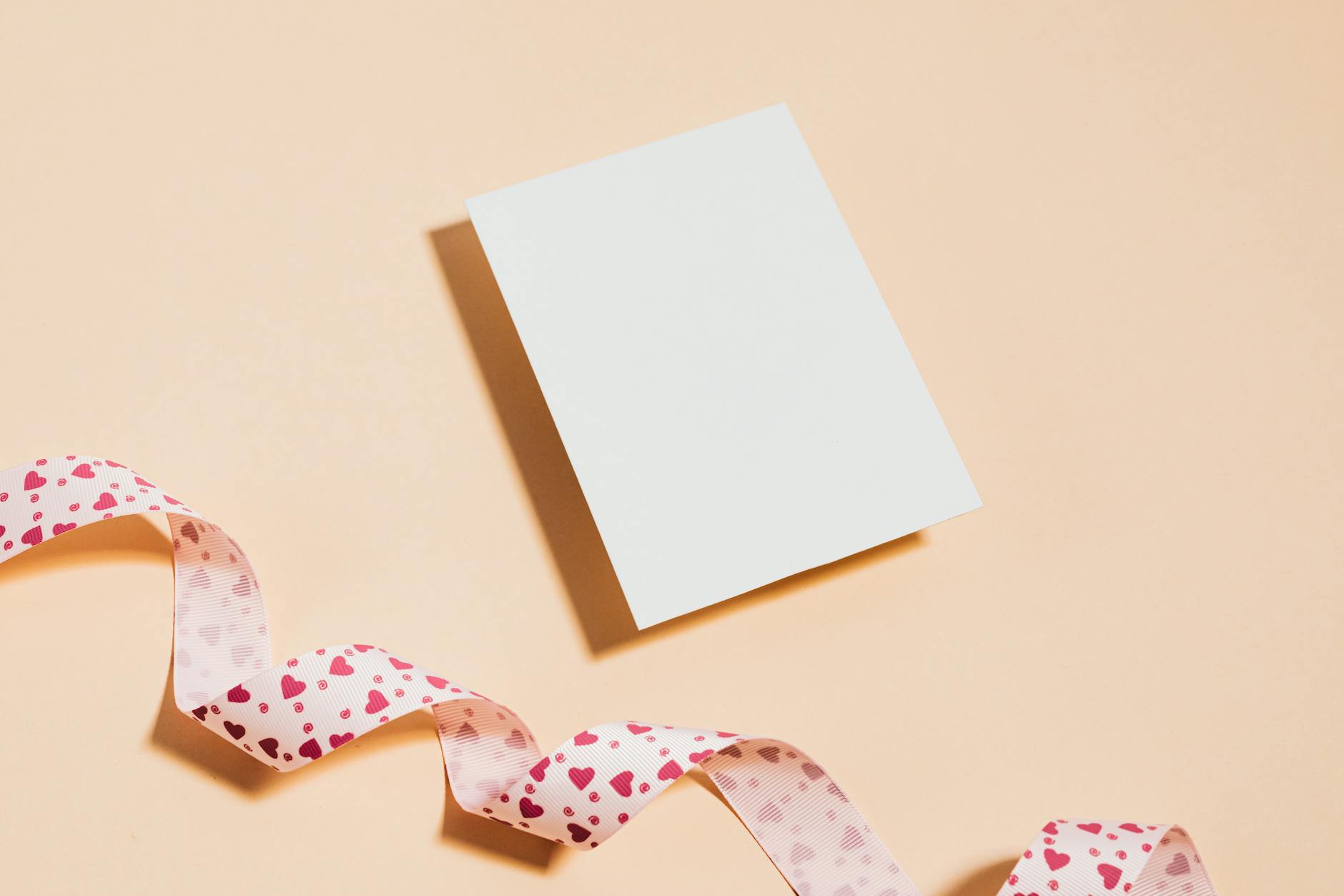 Puste zaproszenie z różową wstążką w serduszka na brzoskwiniowym tle