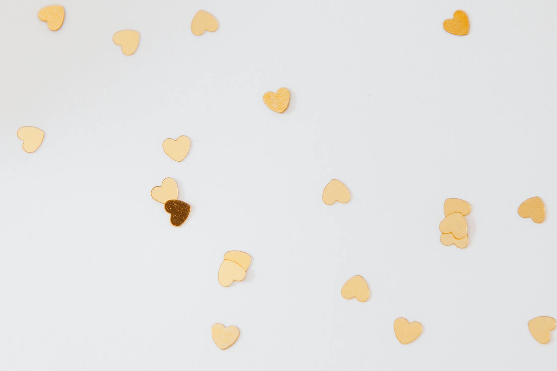Złote konfetti w kształcie serc rozsypane na białym tle